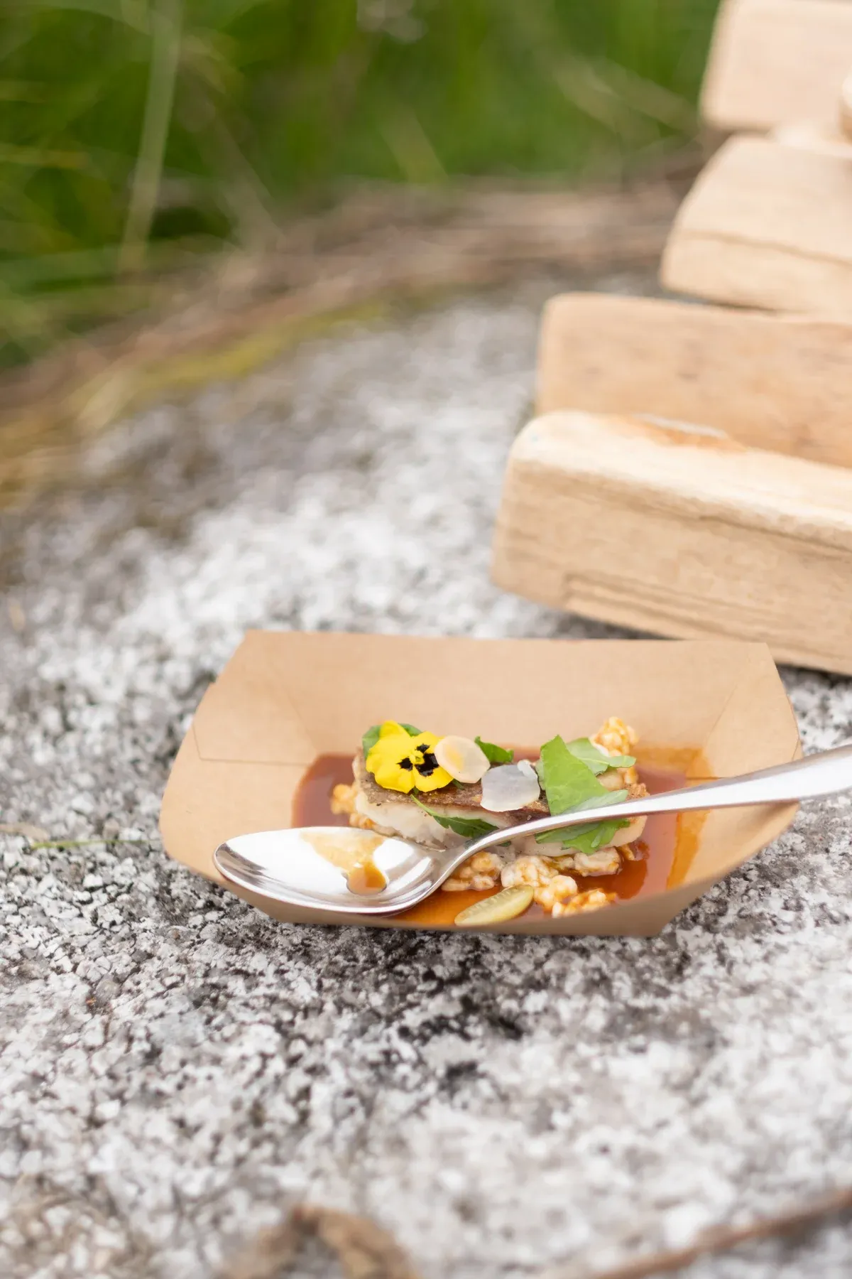 Fingerfood mit essbaren Blüten in Kartonschale auf Granit