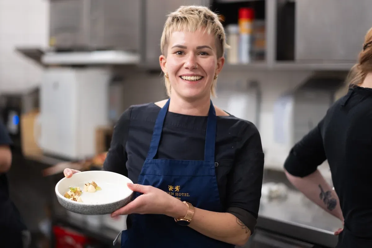 Lachende Köchin präsentiert ein Gericht in der Restaurantküche