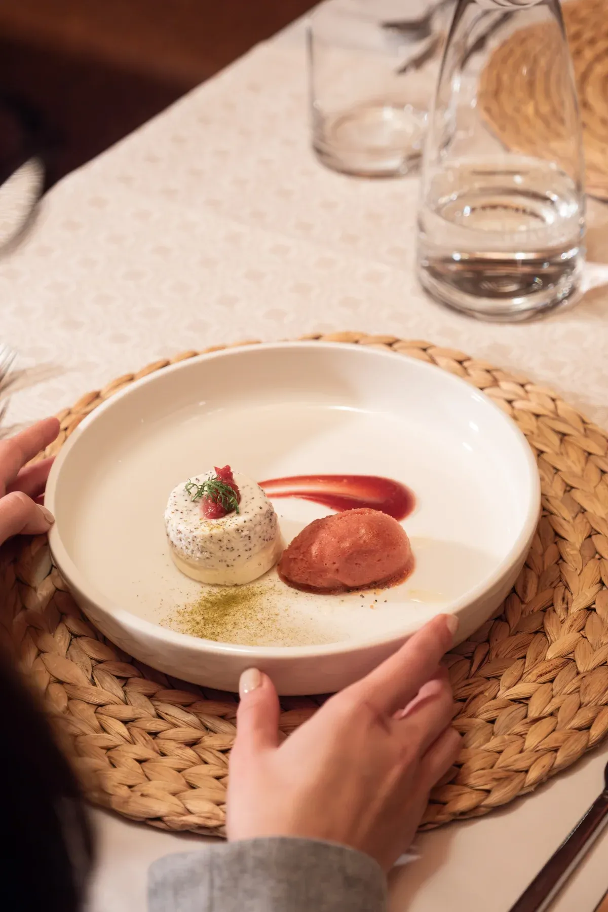 Dessert mit rotem Sorbet auf weißem Teller, Hände der Gästin am Tisch